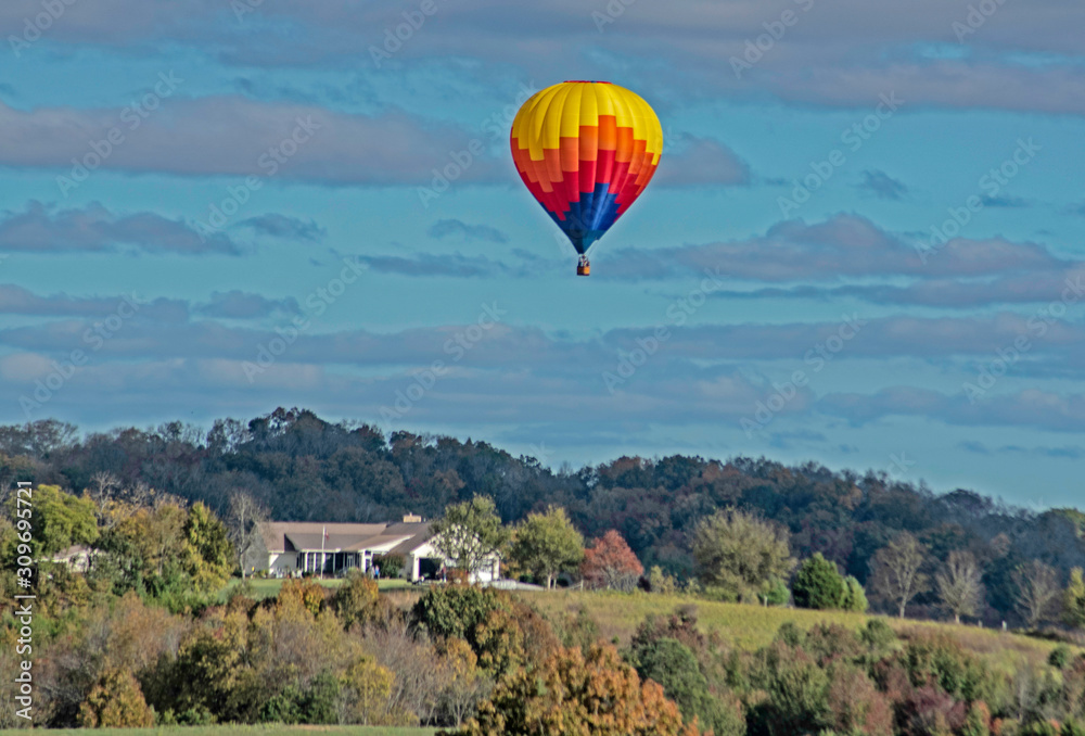 Naklejka premium A single hot air balloon flies over a green valley.