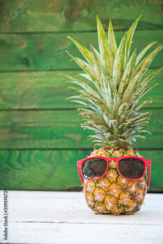 Holiday pineapple have sunglasses on green wooden background