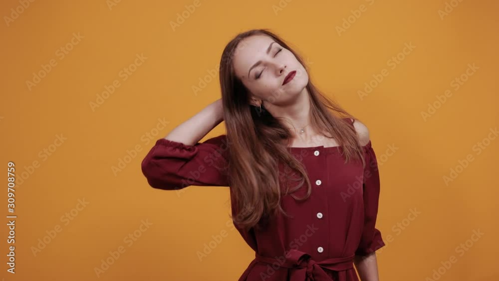 Attractive caucasian woman in maroon dress isolated on orange background in studio relaxing, dancing, stretched muscules. People sincere emotions, lifestyle concept. Attractive caucasian woman in maroon dress isolated on orange background in studio relaxing, dancing, stretched muscules. People sincere emotions, lifestyle concept.