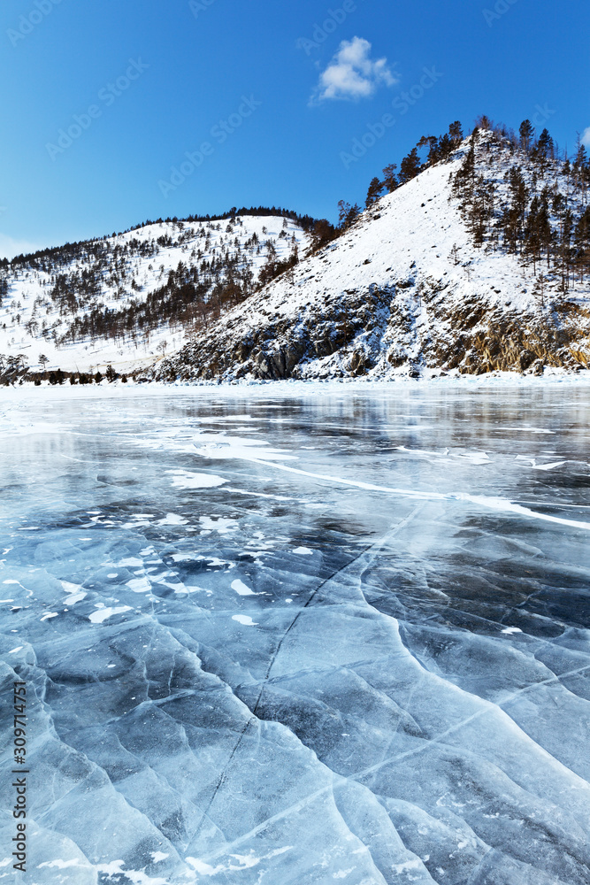 frozen Baikal Lake. Snow-covered hills on the shore of lake and transparent ice with cracks. Beautiful winter landscape. Ice travel. Winter background