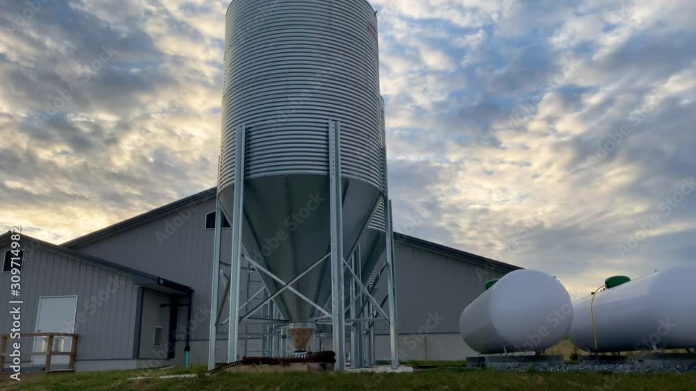Panning shot reveals animal feed bins, propane tanks, hog barn under dramatic sky