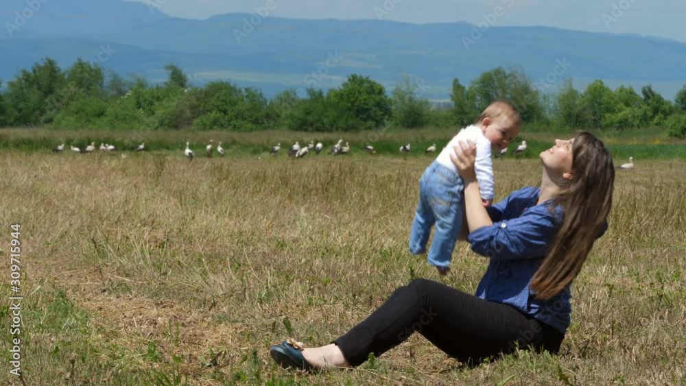 Young mother hold and rise up newborn bay child in a field with many storks Young mother hold and rise up newborn bay child in a field with many storks