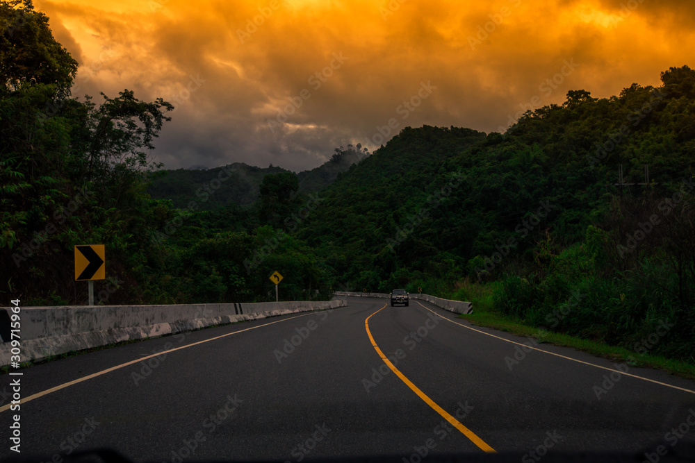 Naklejka premium Blurred background of a mountain road view, from a car windscreen that runs with care, with natural scenery surrounded by plants, large trees