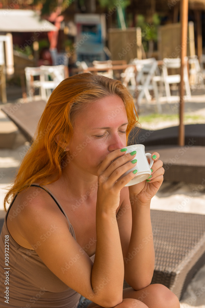 Fototapeta premium Young woman drinking coffee at the beach