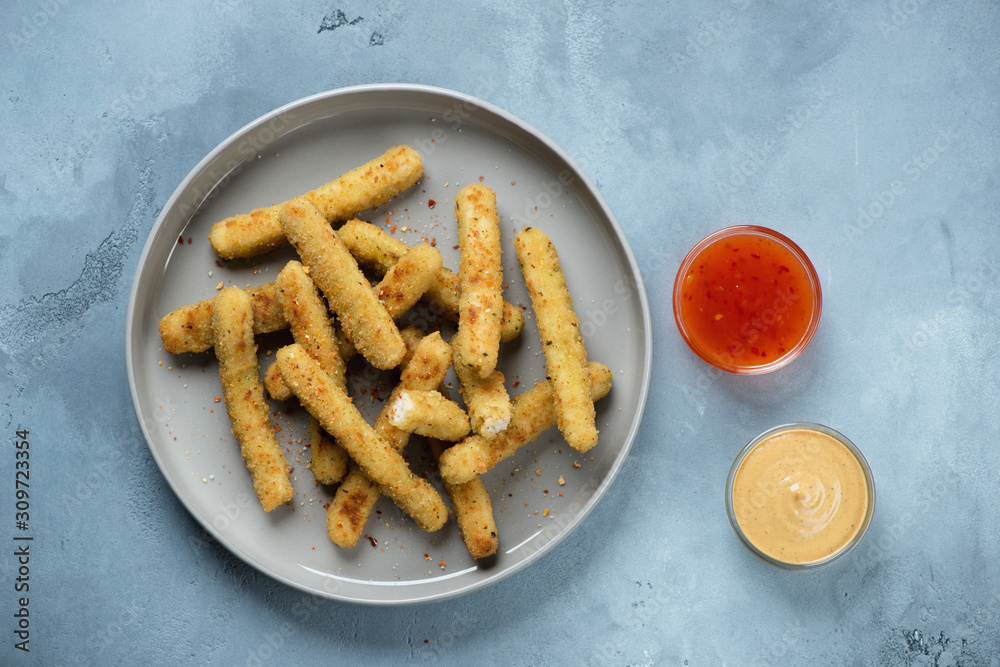 Grey plate with fried breaded chicken sticks and dips, flatlay over grey concrete background, studio shot Grey plate with fried breaded chicken sticks and dips, flatlay over grey concrete background, studio shot