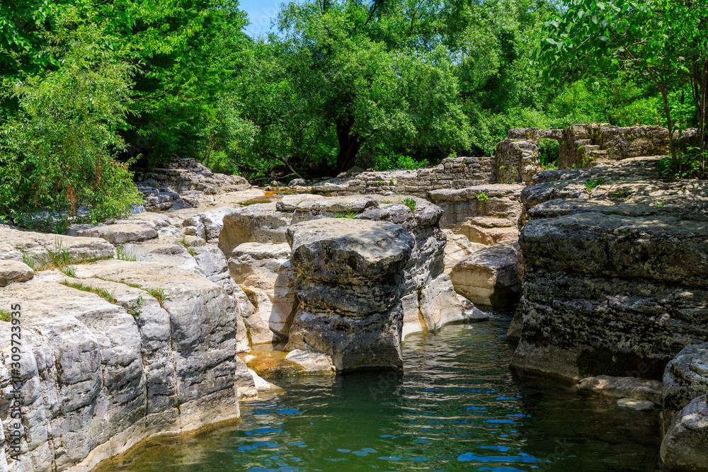 Okatse first canyon and small Kinchkha waterfall in the canyon of the river Okatse. Rest in Georgia. Rocky ledges of the mountain with green trees. Okatse first canyon and small Kinchkha waterfall in the canyon of the river Okatse. Rest in Georgia. Rocky ledges of the mountain with green trees.