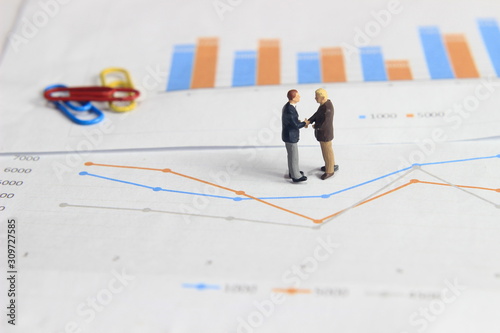 Simple Illustration Photo Two Mini Figure Businessman Toy Handshaking at Graphic Business Chart with colorful paperclip