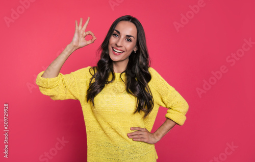 OK mood. Close-up photo of a cheerful woman with long hair  who is smiling while showing ok-sign with her right hand and holding her left hand on a hip.
