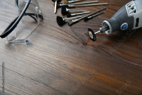 rotary tool with a nozzle for cleaning something on a wooden background. backdrop for repair and cleaning workshop: protective glasses, electric rotary tool and nozzles