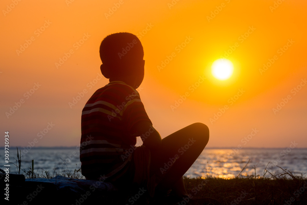 A crippled child sitting at the river watching the sunset. A day ending Sad story.