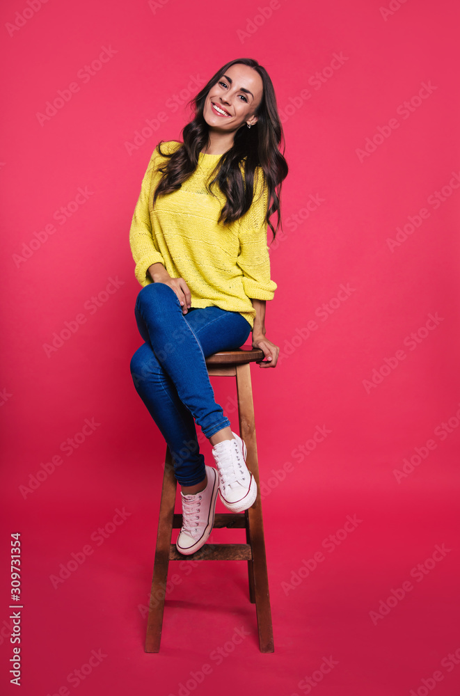 Pure perfection. Full-length photo of a good-looking woman in a yellow sweatshirt, who is posing confidently on a wooden chair with her legs crossed, looking right in the camera lens. Pure perfection. Full-length photo of a good-looking woman in a yellow sweatshirt, who is posing confidently on a wooden chair with her legs crossed, looking right in the camera lens.