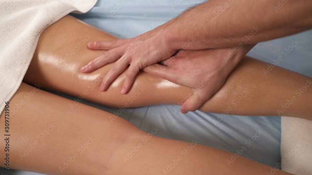 Male practitioner massaging beautiful female leg in spa salon. Young woman enjoying professional massage session. Rehabilitation, medicine, manual therapy, beauty, wellness, health concept Male practitioner massaging beautiful female leg in spa salon. Young woman enjoying professional massage session. Rehabilitation, medicine, manual therapy, beauty, wellness, health concept