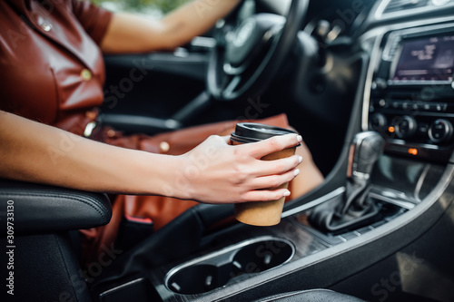 Young woman hands with coffee to go driving her car, close up photo. © Тарас Нагирняк