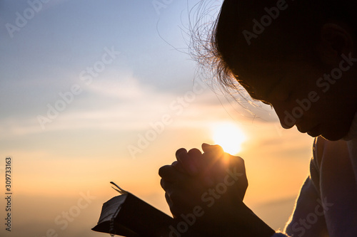 Quadro su tela Silhouette of christian young woman praying with a  cross and open the bible at sunrise, Christian Religion concept background