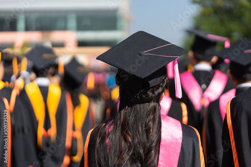 Rear view and soft selective focus of the graduates in the graduation commencement ceremony recieving diploma degree certificate.