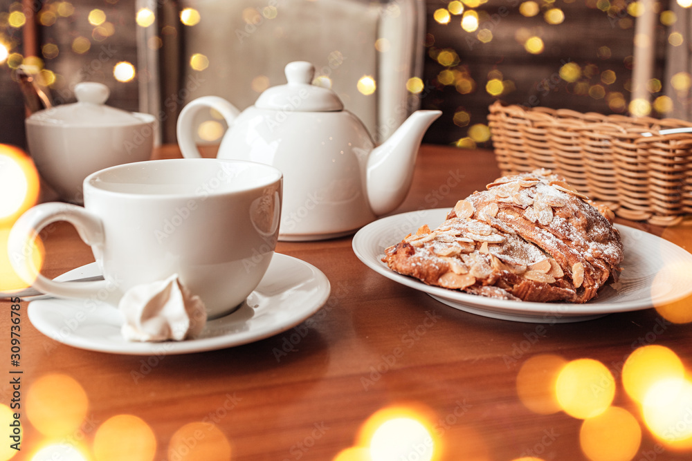 White cup, tea pot and croissant on table in cafe White cup, tea pot and croissant on table in cafe