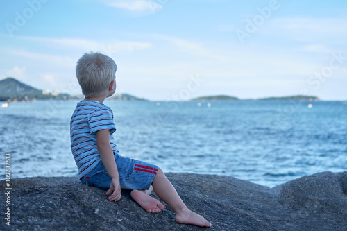 Wallpaper Mural Portrait of little handsome boy sitting on rock near sea water, looking dreamily into the distance. Thailand Torontodigital.ca