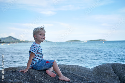 Wallpaper Mural Portrait of little handsome boy sitting on rock near sea water, sad look, Thailand Torontodigital.ca