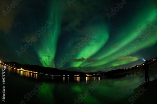 aurora boreal en Lofoten Noruega con persona a la derecha y casa al fondo
