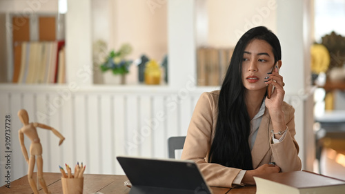 Young woman calling on cell phone in creative work desk.