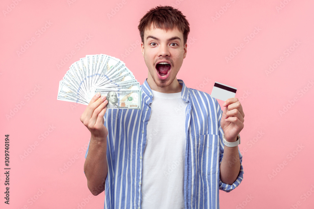 Portrait of overjoyed brunette man with small beard and mustache in casual shirt standing with open mouth and shocked face, holding bank card and cash. indoor studio shot isolated on pink background Portrait of overjoyed brunette man with small beard and mustache in casual shirt standing with open mouth and shocked face, holding bank card and cash. indoor studio shot isolated on pink background