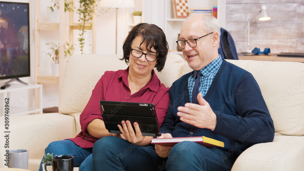 Old couple sitting on sofa during a video call on tablet Old couple sitting on sofa during a video call on tablet