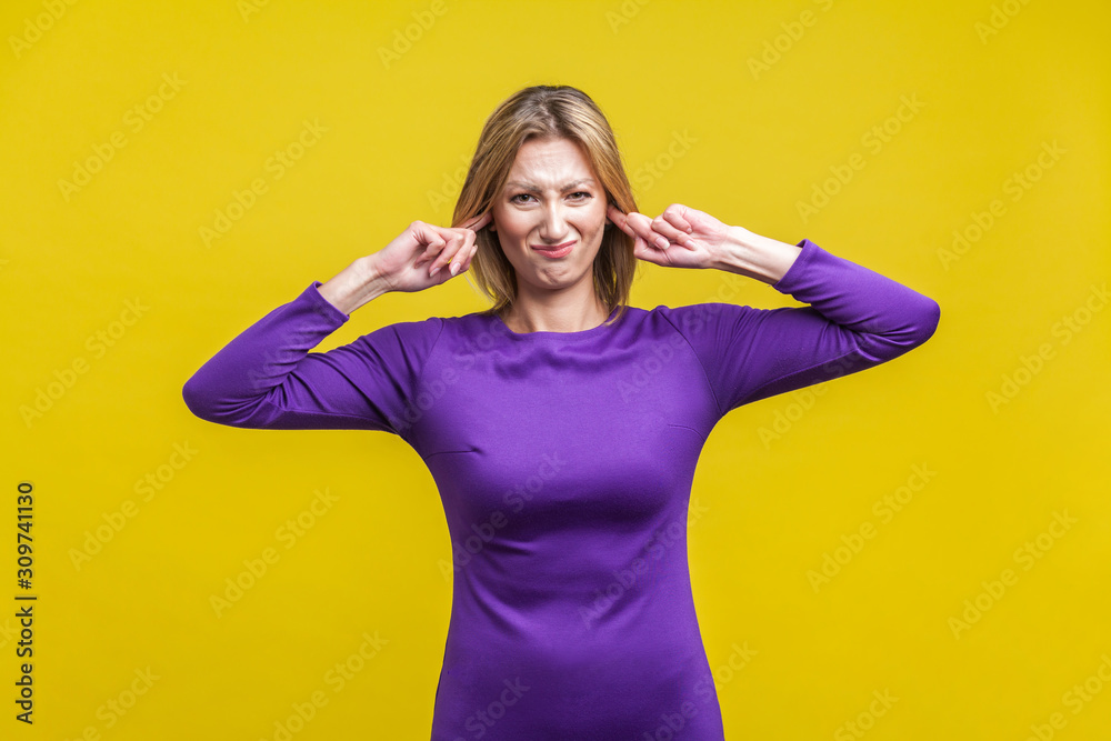 Don't want to hear. Portrait of dissatisfied woman in elegant tight purple dress covering ears with fingers, ignoring loud sound or avoiding conflict. indoor studio shot isolated on yellow background Don't want to hear. Portrait of dissatisfied woman in elegant tight purple dress covering ears with fingers, ignoring loud sound or avoiding conflict. indoor studio shot isolated on yellow background