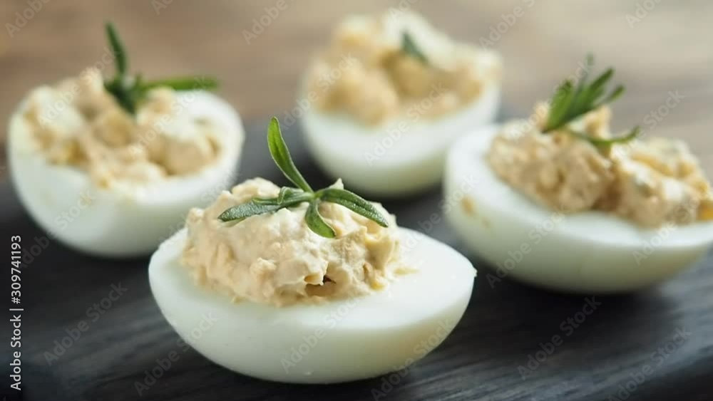 Decoration with fresh rosemary branch stuffed eggs. Close-up of a woman's hand puts greens on the finished dish of boiled stuffed eggs. Decoration with fresh rosemary branch stuffed eggs. Close-up of a woman's hand puts greens on the finished dish of boiled stuffed eggs.