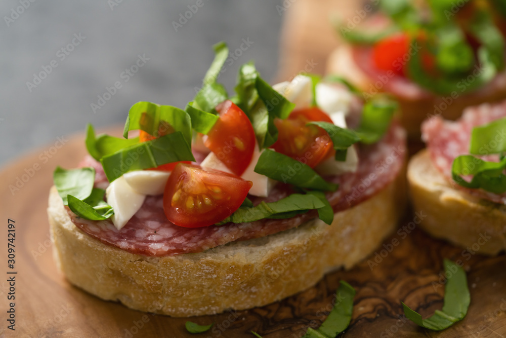 Bruschetta with mozzarella, cherry tomatoes and salame on olive board
