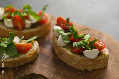 Bruschetta with mozzarella, cherry tomatoes and pesto on olive board