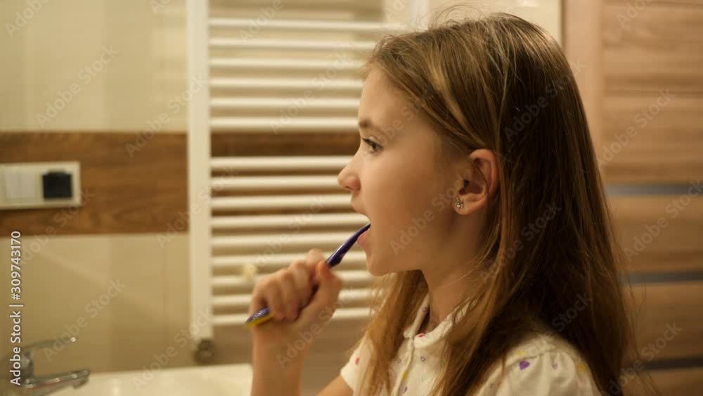 Cute kid girl ten years old brushing her teeth in bathroom at home in pajamas in the evening Cute kid girl ten years old brushing her teeth in bathroom at home in pajamas in the evening