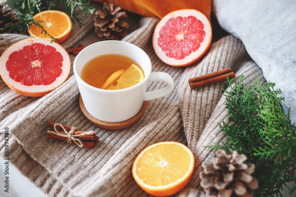 Christmas cozy winter home decor. New year still life: cup of citrus tea, oranges, grapefruits, cinnamon sticks, pine cones, fir branches, knitted sweater. Christmas cozy winter home decor. New year still life: cup of citrus tea, oranges, grapefruits, cinnamon sticks, pine cones, fir branches, knitted sweater.
