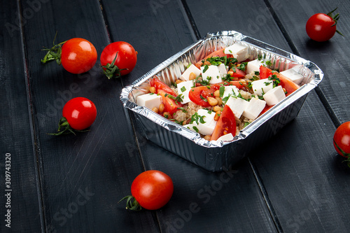 Salad with mozzarella, pine nuts and cherry tomatoes in containers on a dark background. Takeaway. Diet and healthy food.