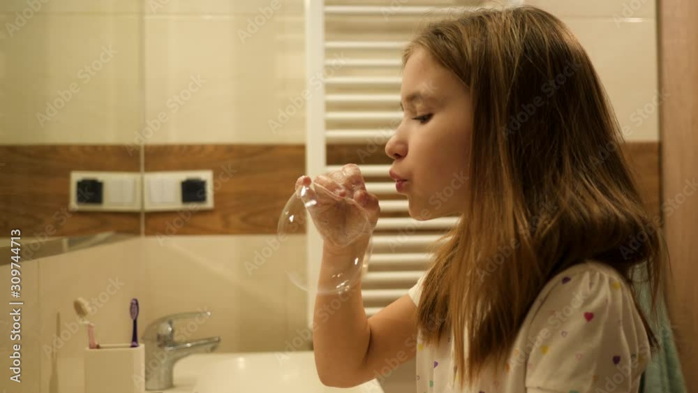 After washing hands cute kid girl play make soap bubbles in bathroom in front of mirror having fun in pajamas in the morning After washing hands cute kid girl play make soap bubbles in bathroom in front of mirror having fun in pajamas in the morning