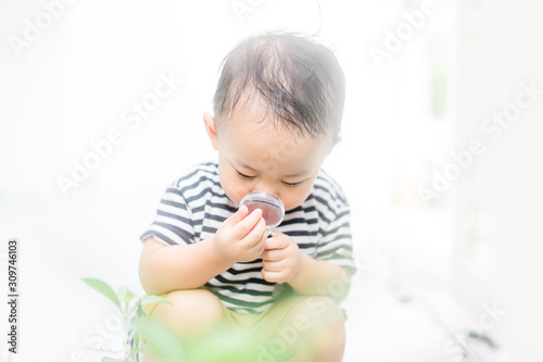 Asian baby boy Looking At green leaf Through Magnifying Glass at home on white Background.Concept for research global warming, global network,SEO search engine and Kid Education of ecology. © MIA Studio