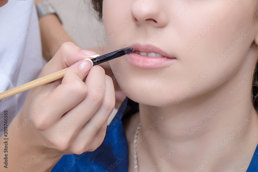 Makeup artist paints girl's lips with a brush Makeup artist paints girl's lips with a brush