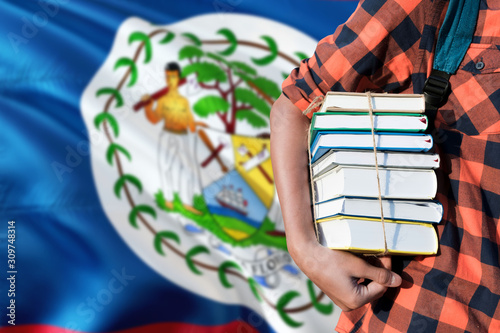 Belize national education concept. Close up of teenage student holding books under his arm with country flag background.