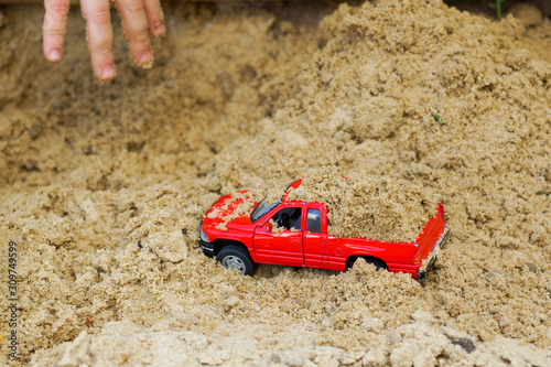 child buries sand in red toy car