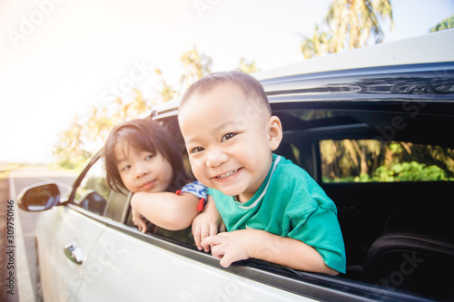 Happy siblings laughing and smiling near window go travel by car against blue sky and coconut trees.Summer road trip, Family with children in car.