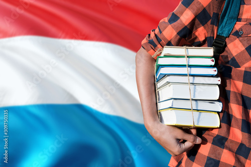 Luxembourg national education concept. Close up of teenage student holding books under his arm with country flag background. © sezerozger