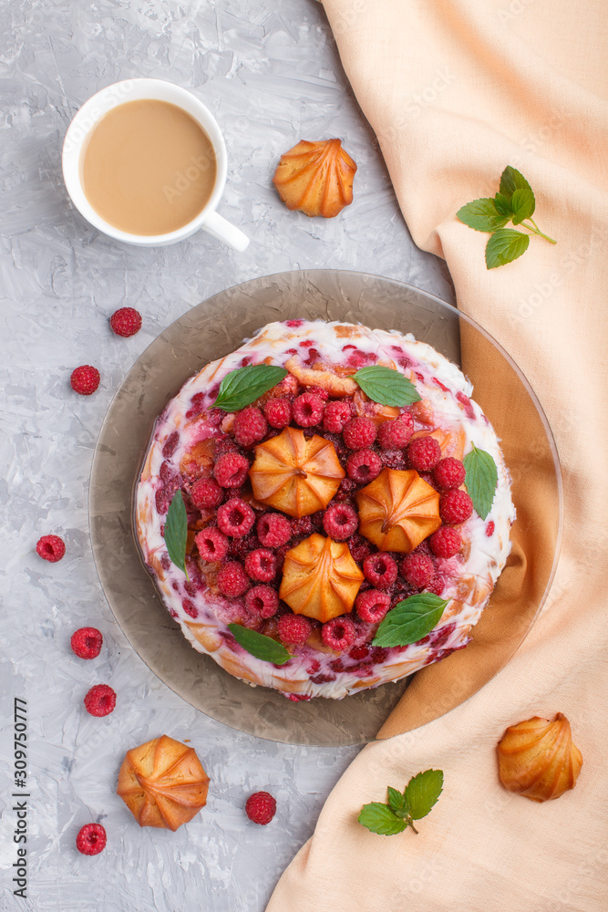 Homemade jelly cake with milk, cookies and raspberry on a gray concrete  background with cup of coffee and orange textile, top view.