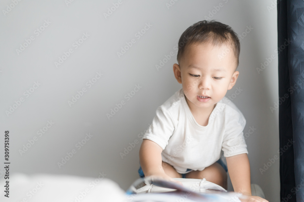 2 years little asian toddler boy in white t-shirt reading bible picture story for kid in the morning.Hands holding on a Holy Bible in bed room concept for Education bible study, faith and religion. 2 years little asian toddler boy in white t-shirt reading bible picture story for kid in the morning.Hands holding on a Holy Bible in bed room concept for Education bible study, faith and religion.