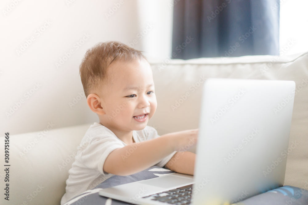 Portrait of a little toddler boy watching laptop and exciting face.Little asian boy child with laptop computer or notebook in living room at home.E Learning, Shopping online concept. Portrait of a little toddler boy watching laptop and exciting face.Little asian boy child with laptop computer or notebook in living room at home.E Learning, Shopping online concept.