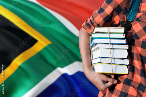 South Africa national education concept. Close up of teenage student holding books under his arm with country flag background.