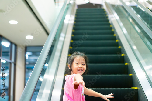 Smiling little child girl walking to escalator alone at mall.First time for little asian girl with escalator.