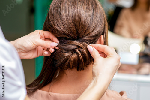 Rear view of hairdresser hands making hairdo for woman in beauty salon.