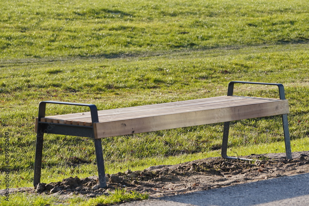modern wooden empty bench by the road in the Park on a Sunny day. a place to relax while walking. modern wooden empty bench by the road in the Park on a Sunny day. a place to relax while walking.