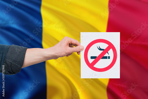 Chad health concept. Hand holding paper with no smoking sign over national waving flag. Quit smoke theme.