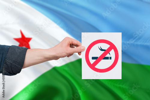 Djibouti health concept. Hand holding paper with no smoking sign over national waving flag. Quit smoke theme.