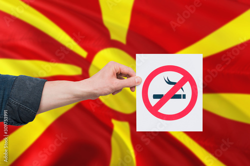 Macedonia health concept. Hand holding paper with no smoking sign over national waving flag. Quit smoke theme.